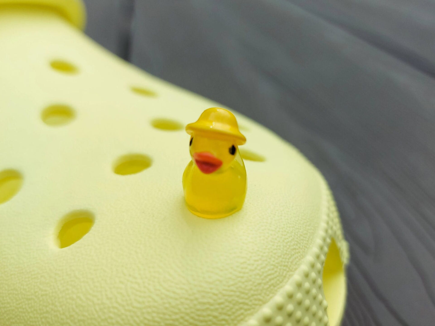 Glow in the dark duck charms wearing bucket hats on a yellow shoes shoe. These colorful charms are available in pink, white, blue, green, yellow, turquoise, peach and purple. The hats all have different colors.