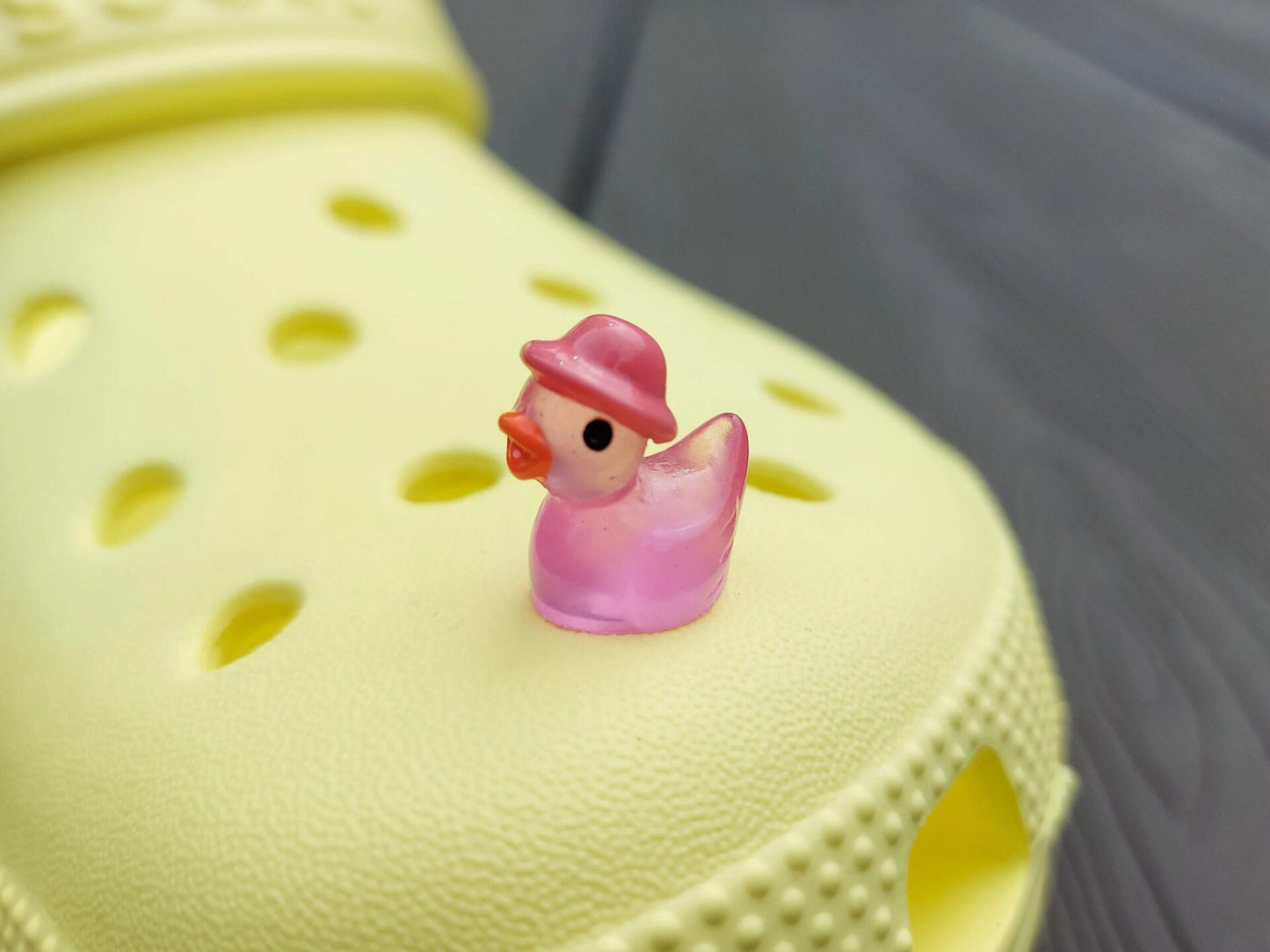 Glow in the dark duck charms wearing bucket hats on a yellow shoes shoe. These colorful charms are available in pink, white, blue, green, yellow, turquoise, peach and purple. The hats all have different colors.