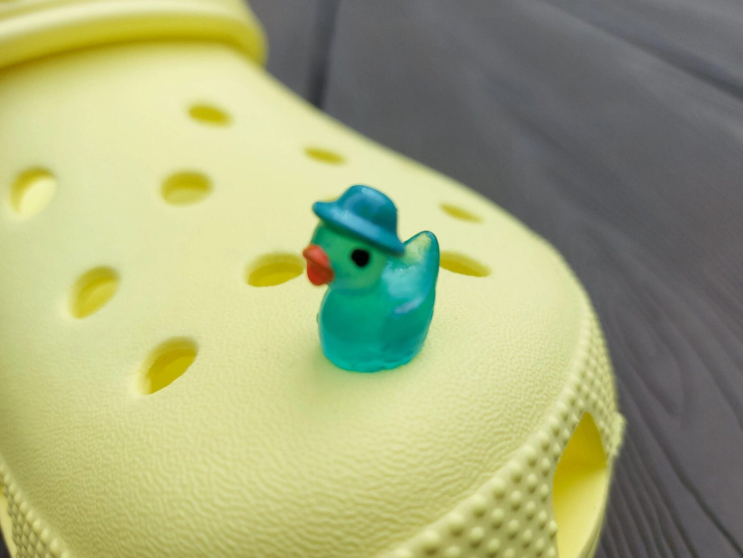 Glow in the dark duck charms wearing bucket hats on a yellow shoes shoe. These colorful charms are available in pink, white, blue, green, yellow, turquoise, peach and purple. The hats all have different colors.