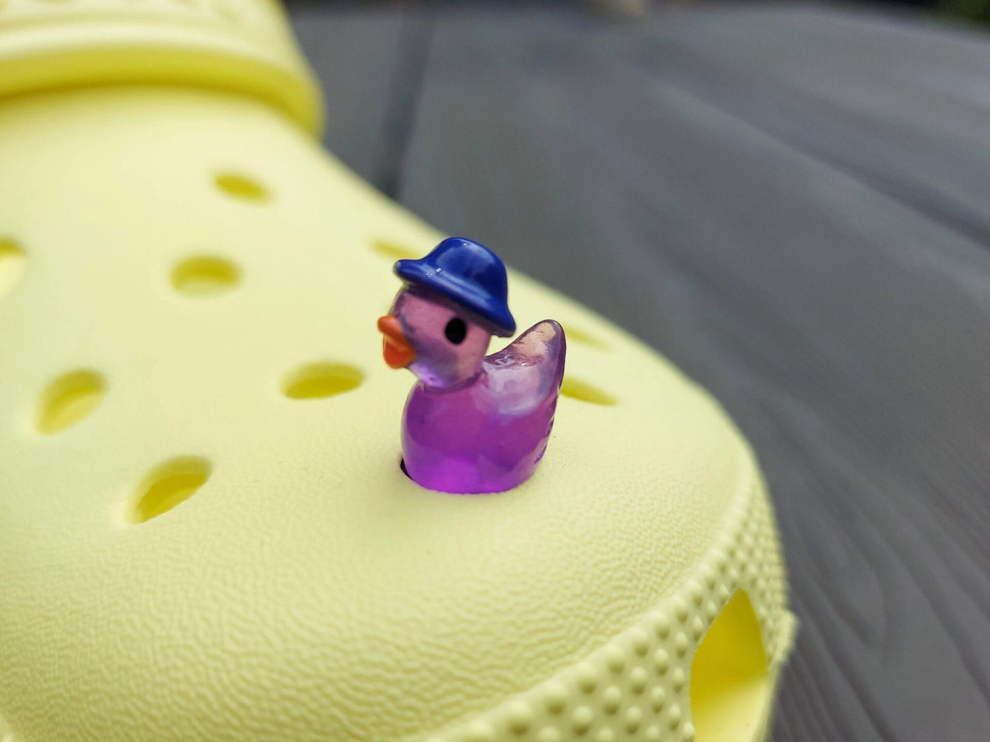 Glow in the dark duck charms wearing bucket hats on a yellow shoes shoe. These colorful charms are available in pink, white, blue, green, yellow, turquoise, peach and purple. The hats all have different colors.