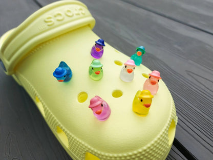 Glow in the dark duck charms wearing bucket hats on a yellow clog shoe. These colorful charms are available in pink, white, blue, green, yellow, turquoise, peach and purple. The hats all have different colors.