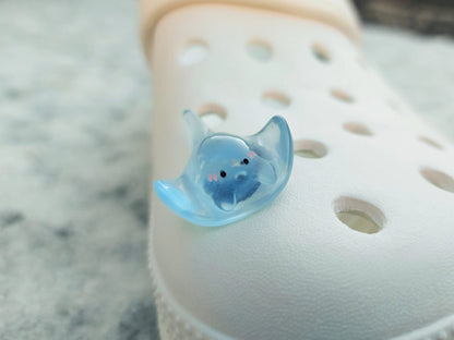 Glow-in-the-dark manta ray charms on a shoe shoe. These enchanting accessories light up in the dark, adding a marine-inspired touch to your footwear. Perfect for customizing your shoes with a unique and magical ocean theme.