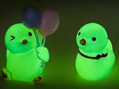 Set of glow in the dark duck charms on a white shoes shoe. All 5 of these ducks each have unique positions and features such as lying down, sitting and holding a bundle of colorful balloons.