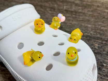 Set of glow in the dark duck charms on a white shoes shoe. All 5 of these ducks each have unique positions and features such as lying down, sitting and holding a bundle of colorful balloons.