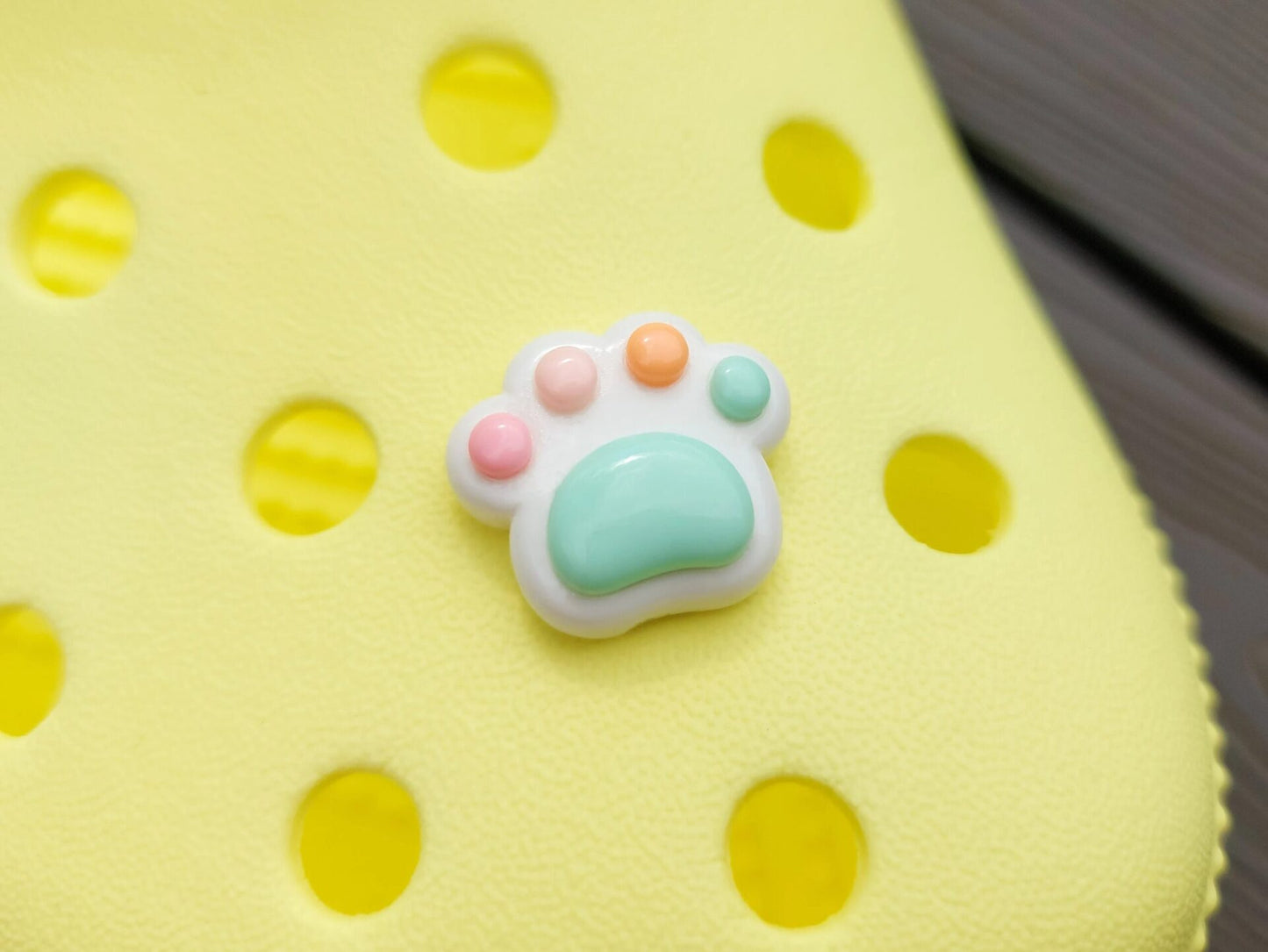 White pawprint charms with pastel-colored footpads on a yellow pair of shoes. These adorable accessories add a cute and playful touch to your footwear, perfect for customizing your shoes with a fun, pet-inspired design.