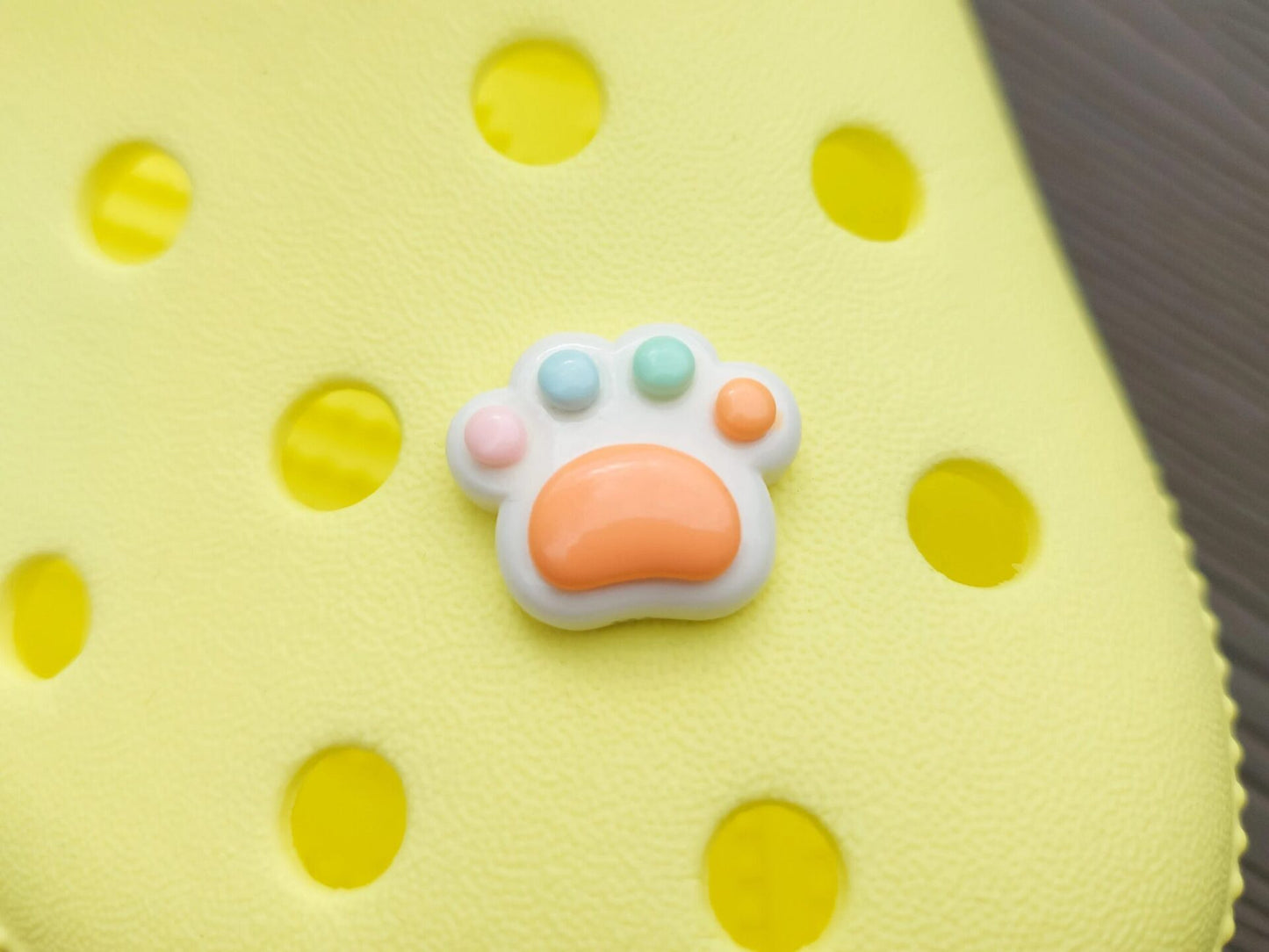 White pawprint charms with pastel-colored footpads on a yellow pair of shoes. These adorable accessories add a cute and playful touch to your footwear, perfect for customizing your shoes with a fun, pet-inspired design.