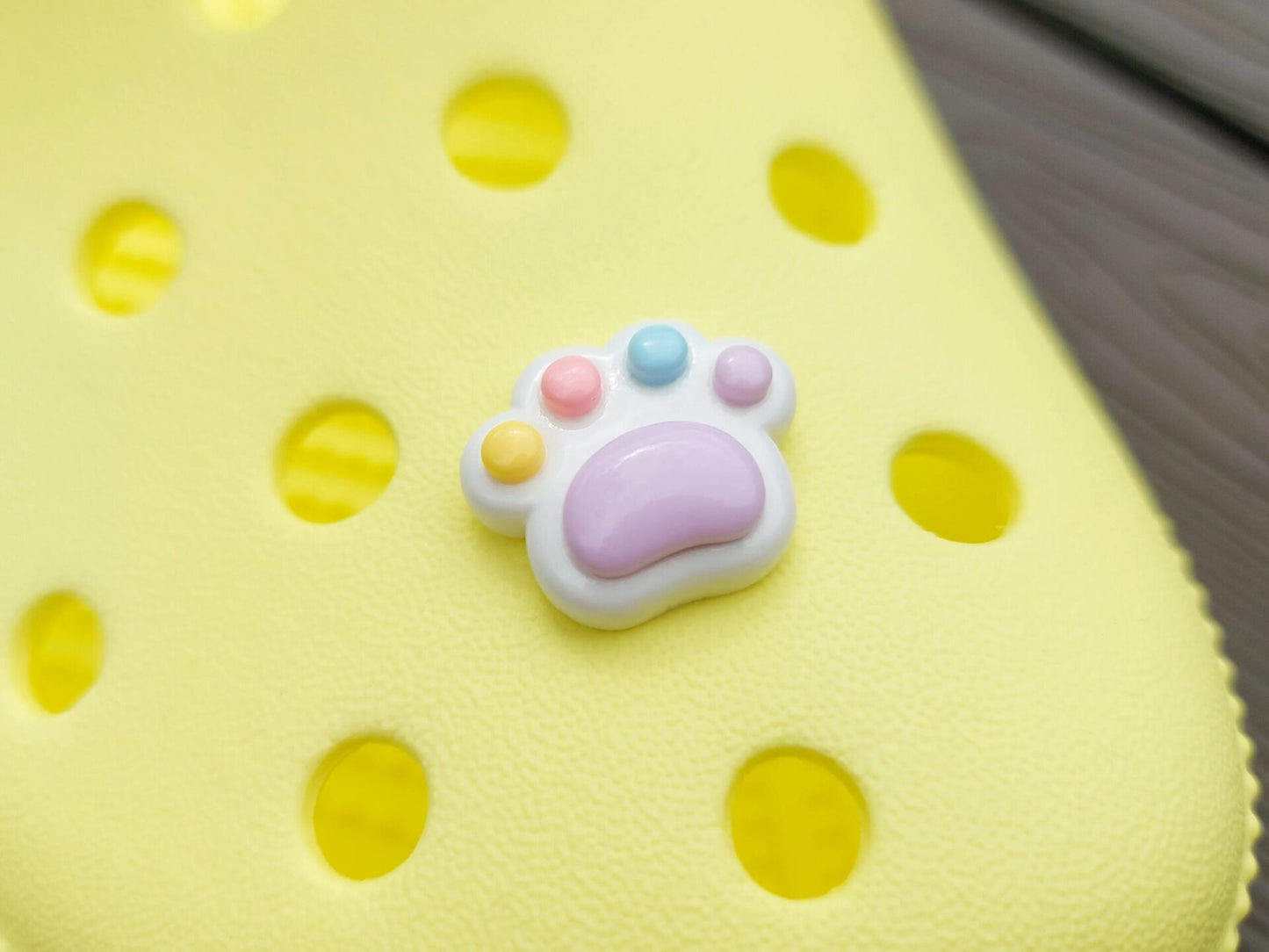 White pawprint charms with pastel-colored footpads on a yellow pair of shoes. These adorable accessories add a cute and playful touch to your footwear, perfect for customizing your shoes with a fun, pet-inspired design.