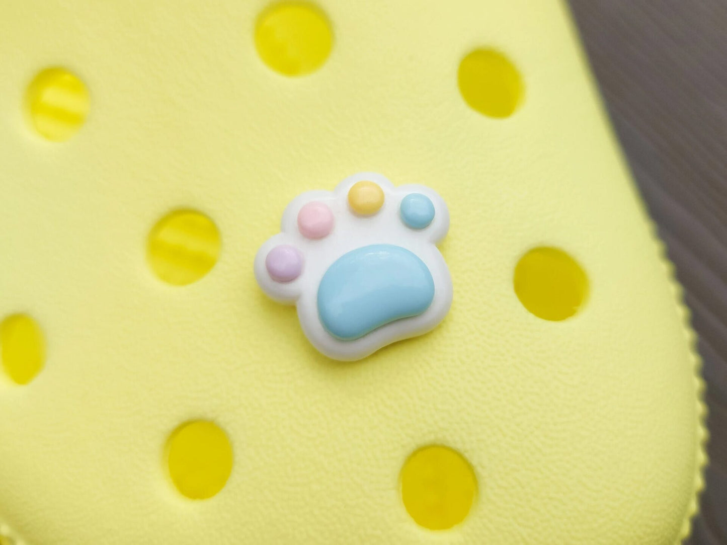 White pawprint charms with pastel-colored footpads on a yellow pair of shoes. These adorable accessories add a cute and playful touch to your footwear, perfect for customizing your shoes with a fun, pet-inspired design.