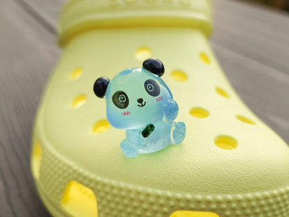 Set of glow in the dark panda shoe charms displayed on a shoe shoe. The charms feature small panda bears in various colors, with a glowing effect. These adorable accessories are designed to light up in the dark.