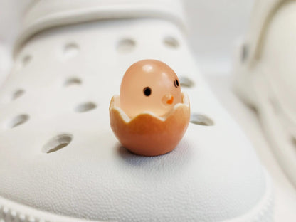 A collection of glow-in-the-dark shoe charms featuring adorable baby chicks nestled in colorful egg shells. Each charm showcases a bright chick in a variety of soft, pastel hues, perfect for adding a fun and playful glow to your shoes at night.