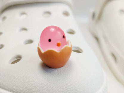 A collection of glow-in-the-dark shoe charms featuring adorable baby chicks nestled in colorful egg shells. Each charm showcases a bright chick in a variety of soft, pastel hues, perfect for adding a fun and playful glow to your shoes at night.