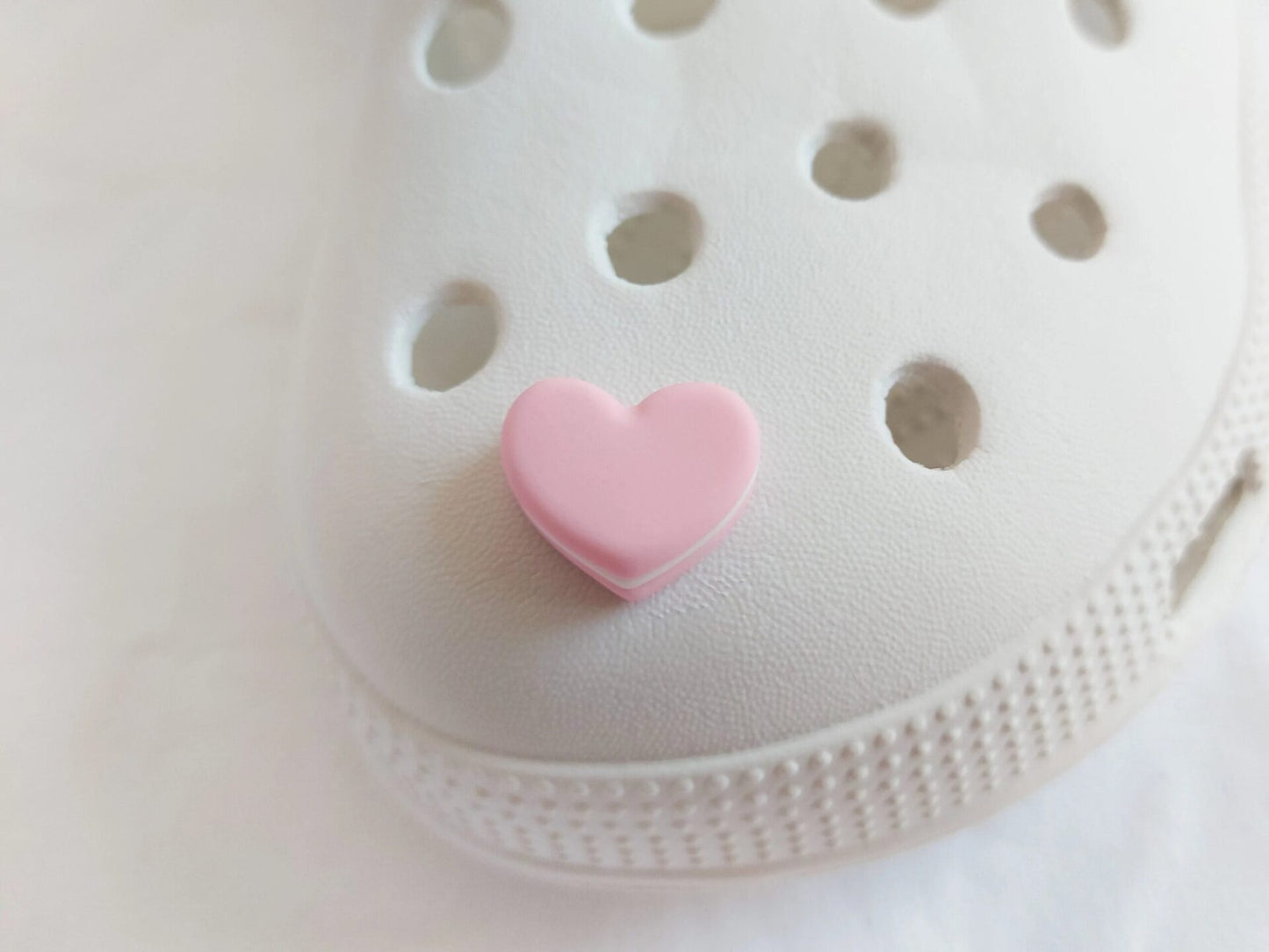 Yellow shoes adorned with pastel-colored macaron heart charms, placed among vibrant pink flowers. The charms add a playful and loving touch to the shoes.