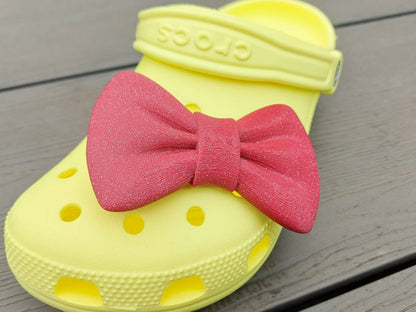 3d-printed bow shoe charms on a pair of shoes shoes. Multiple colors and they have a sparkly glitter.