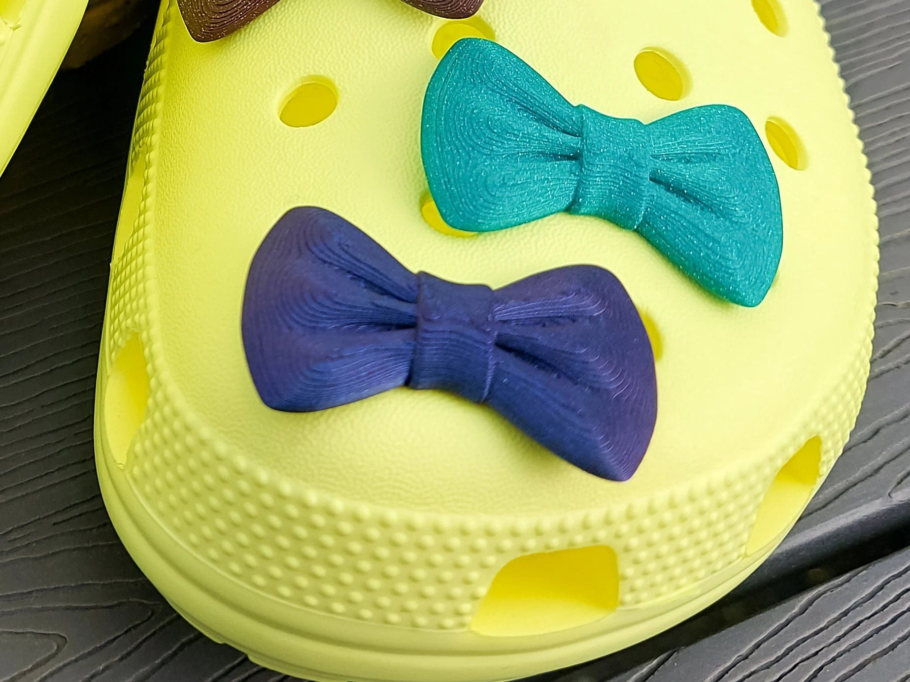 3d-printed bow shoe charms on a pair of shoes shoes. Multiple colors and they have a sparkly glitter.