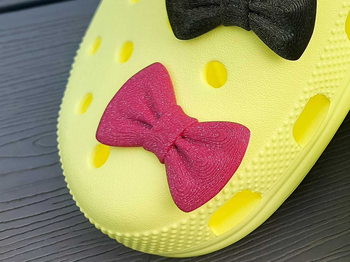 3d-printed bow shoe charms on a pair of shoes shoes. Multiple colors and they have a sparkly glitter.
