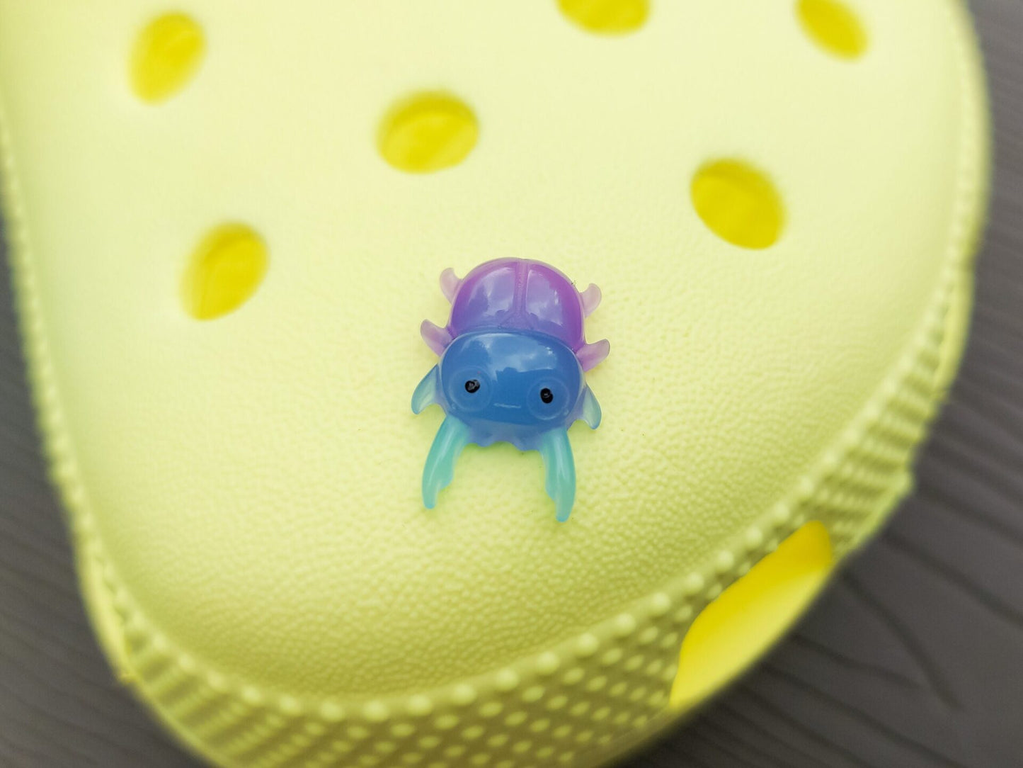 A vibrant collection of beetle-themed shoe charms decorates a yellow shoes shoe. The charms feature detailed, multicolored beetles in various shades, adding a playful yet nature-inspired vibe to the footwear.