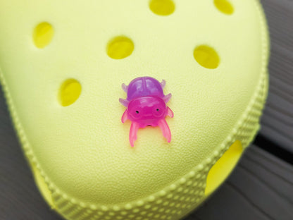 A vibrant collection of beetle-themed shoe charms decorates a yellow shoes shoe. The charms feature detailed, multicolored beetles in various shades, adding a playful yet nature-inspired vibe to the footwear.