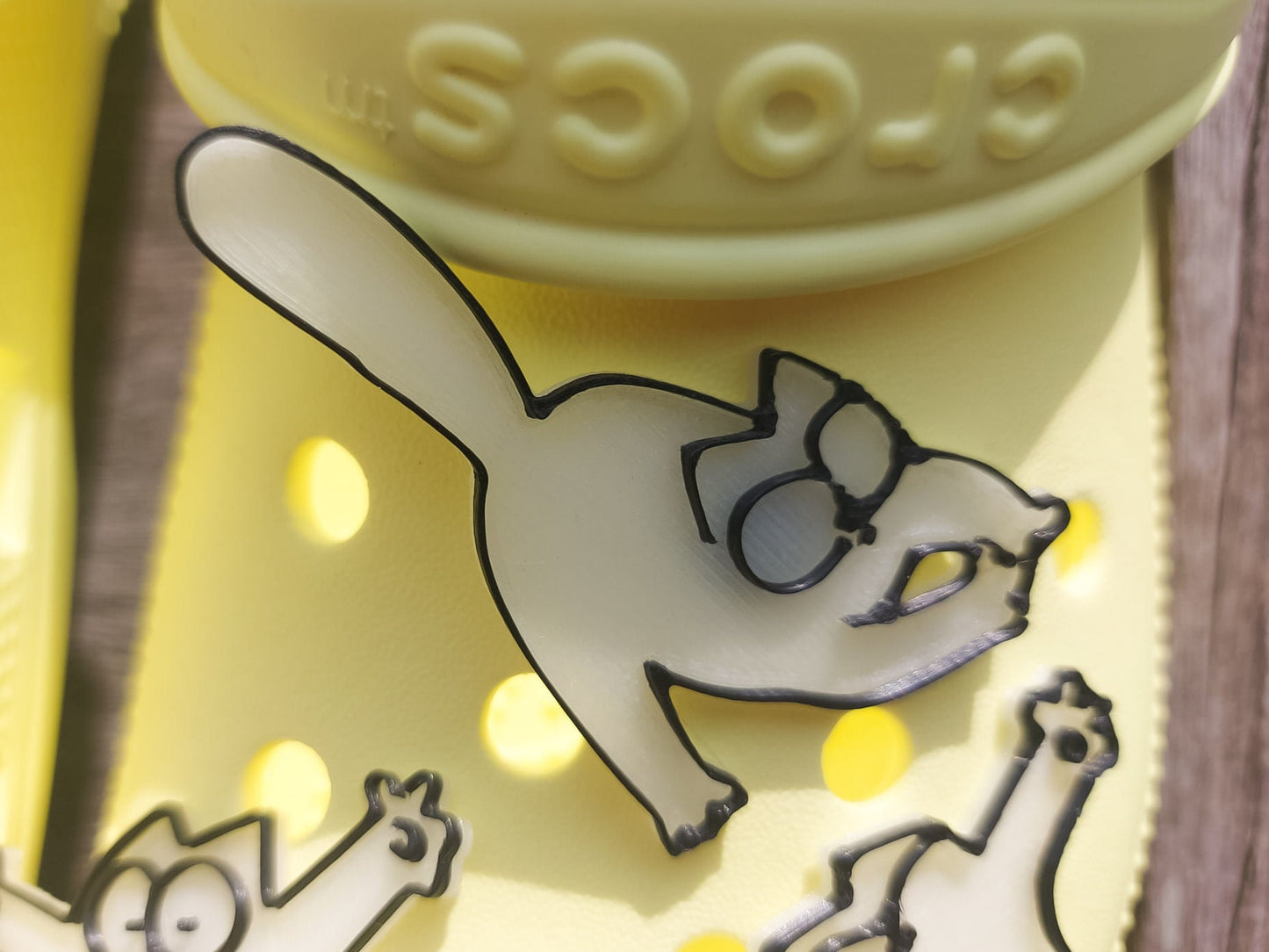 Various 3d-printed cartoon cat shoe charms that glow in the dark on a pair of yellow shoes. Each cat has unique features and expressions.
