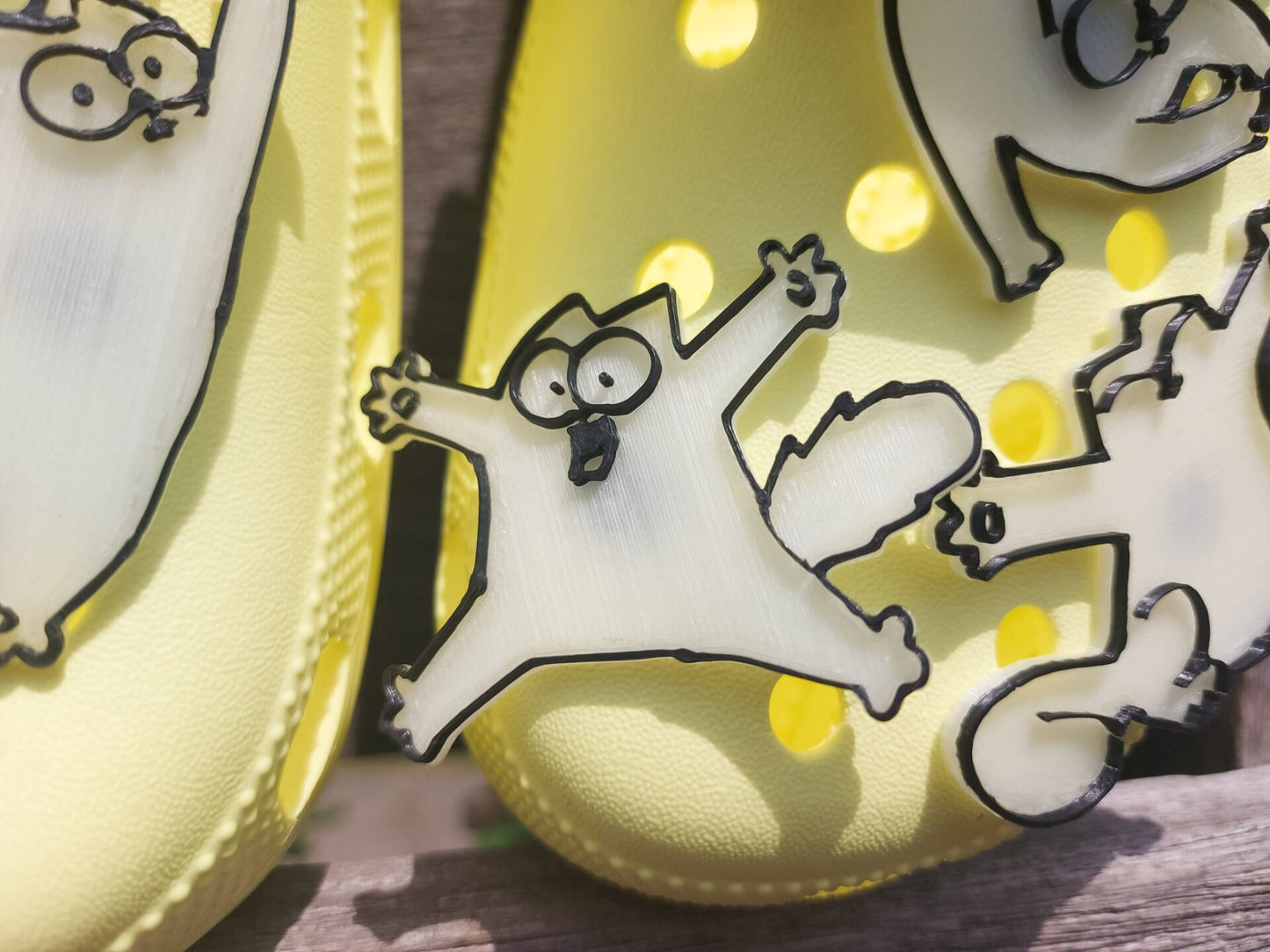 Various 3d-printed cartoon cat shoe charms that glow in the dark on a pair of yellow shoes. Each cat has unique features and expressions.