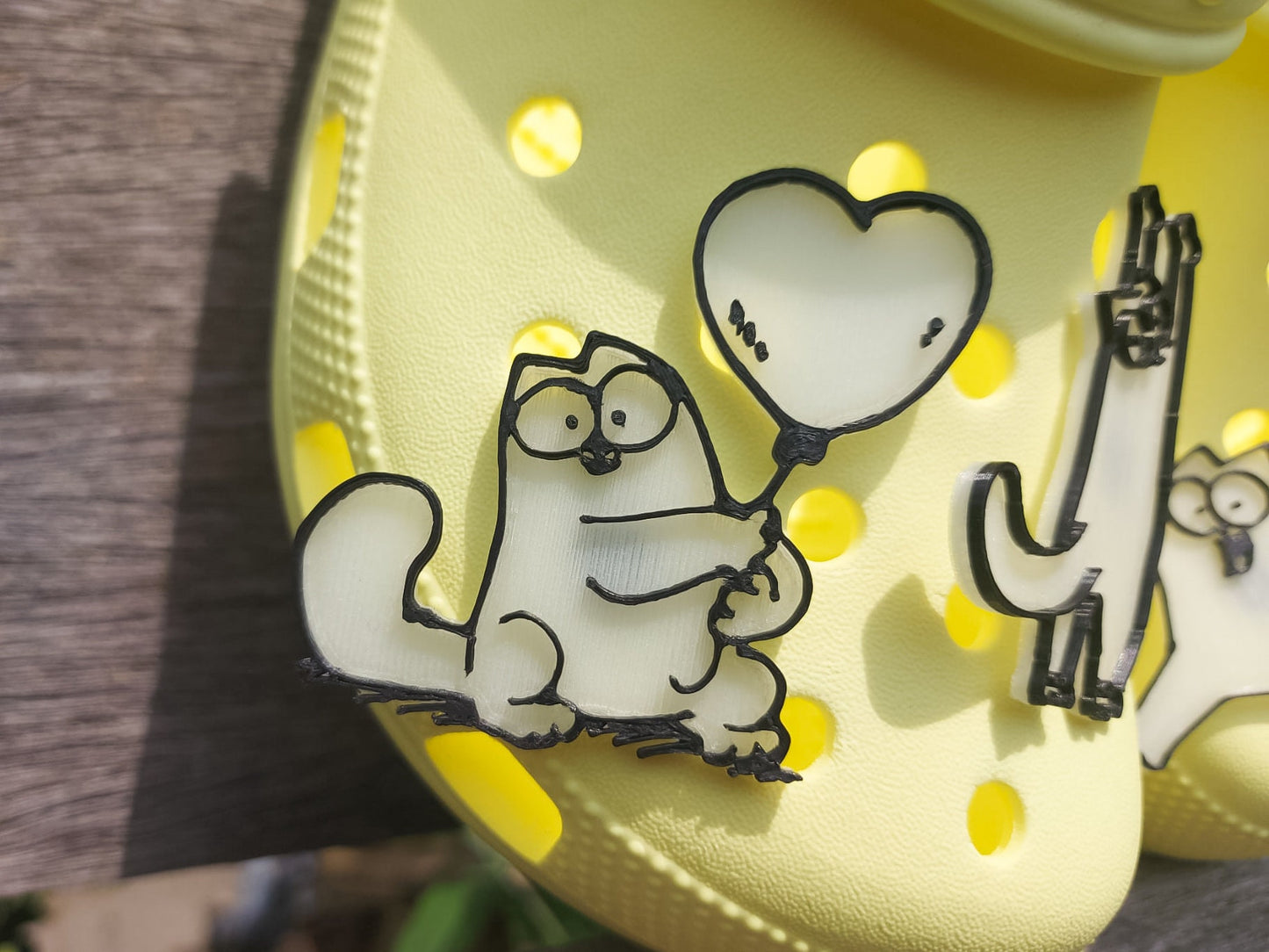 Various 3d-printed cartoon cat shoe charms that glow in the dark on a pair of yellow shoes. Each cat has unique features and expressions.