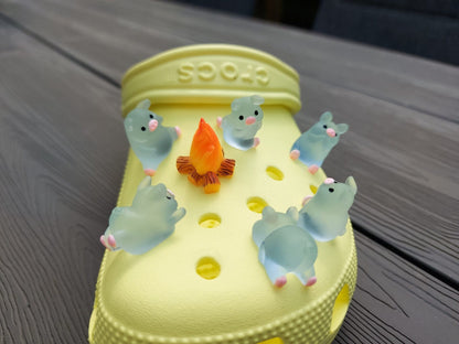 Set of glow-in-the-dark shoe charms featuring adorable pigs around a campfire on a shoe shoe. These playful accessories light up in the dark, adding a unique and whimsical touch to your footwear, perfect for personalizing your shoes.