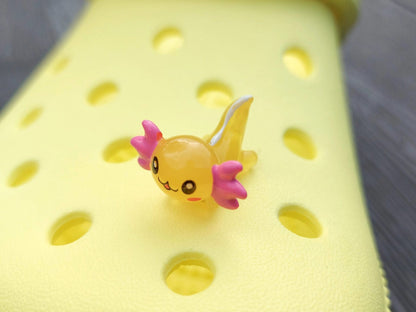 Colorful axolotl charms on a pair of yellow shoes shoes. The axolotls are blue, purple, green, orange, yellow and pink and have cute, smiling faces.