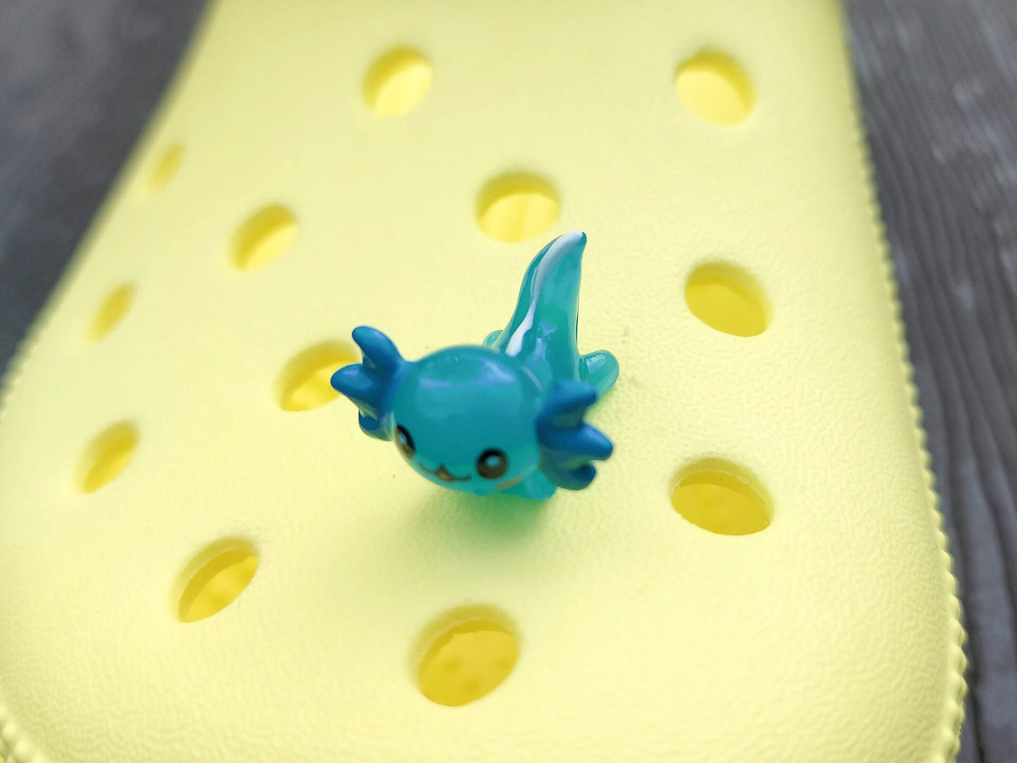 Colorful axolotl charms on a pair of yellow shoes shoes. The axolotls are blue, purple, green, orange, yellow and pink and have cute, smiling faces.