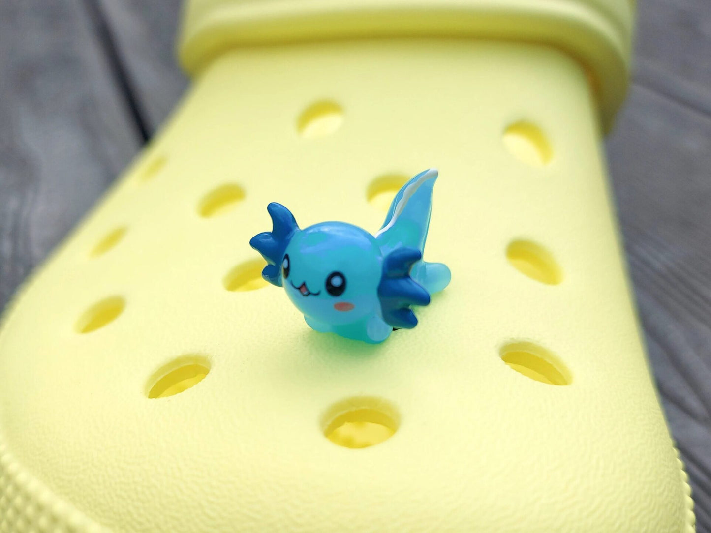 Colorful axolotl charms on a pair of yellow shoes shoes. The axolotls are blue, purple, green, orange, yellow and pink and have cute, smiling faces.
