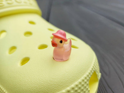 Glow in the dark duck charms wearing bucket hats on a yellow shoes shoe. These colorful charms are available in pink, white, blue, green, yellow, turquoise, peach and purple. The hats all have different colors.