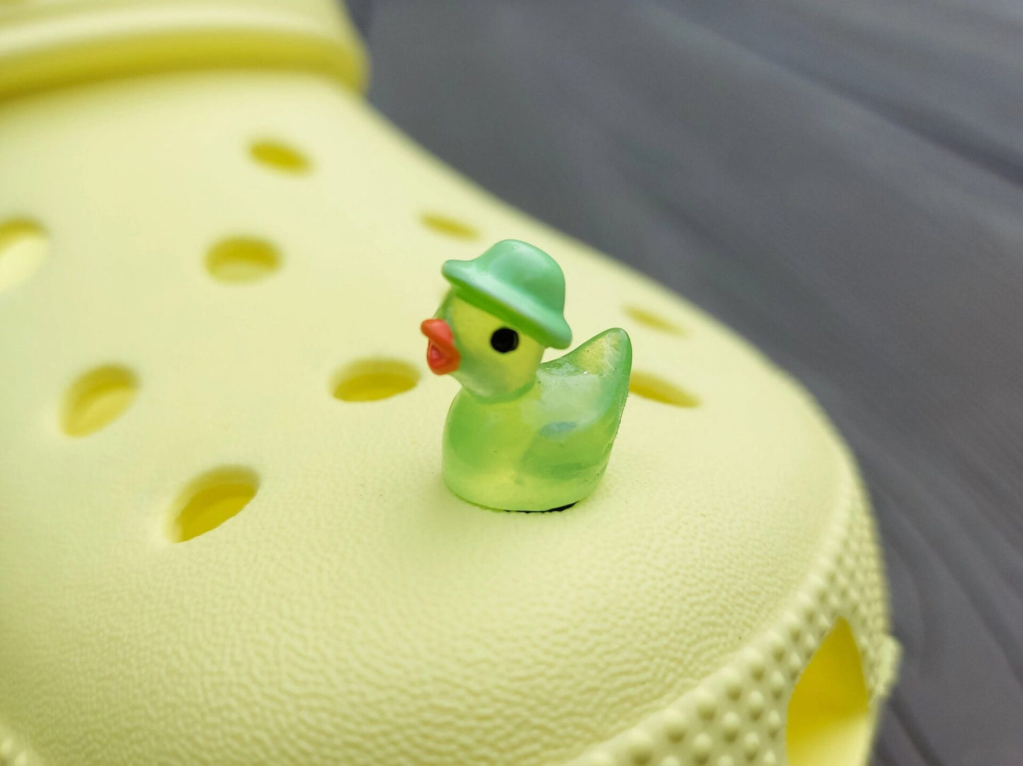Glow in the dark duck charms wearing bucket hats on a yellow shoes shoe. These colorful charms are available in pink, white, blue, green, yellow, turquoise, peach and purple. The hats all have different colors.