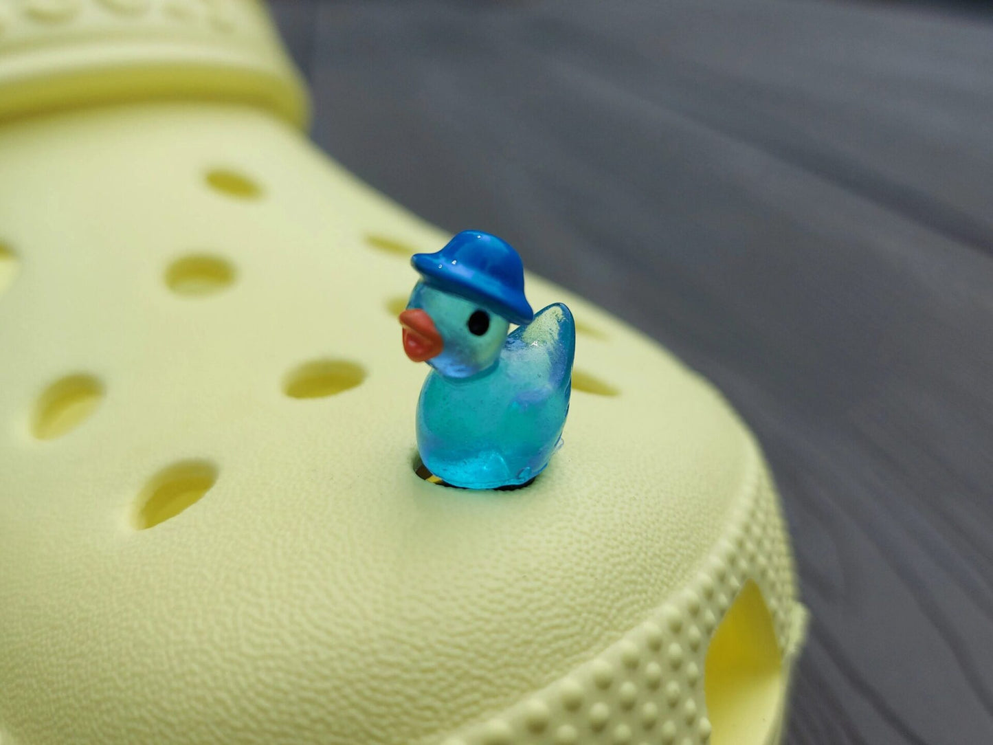 Glow in the dark duck charms wearing bucket hats on a yellow shoes shoe. These colorful charms are available in pink, white, blue, green, yellow, turquoise, peach and purple. The hats all have different colors.