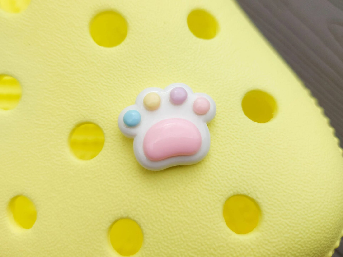 White pawprint charms with pastel-colored footpads on a yellow pair of shoes. These adorable accessories add a cute and playful touch to your footwear, perfect for customizing your shoes with a fun, pet-inspired design.