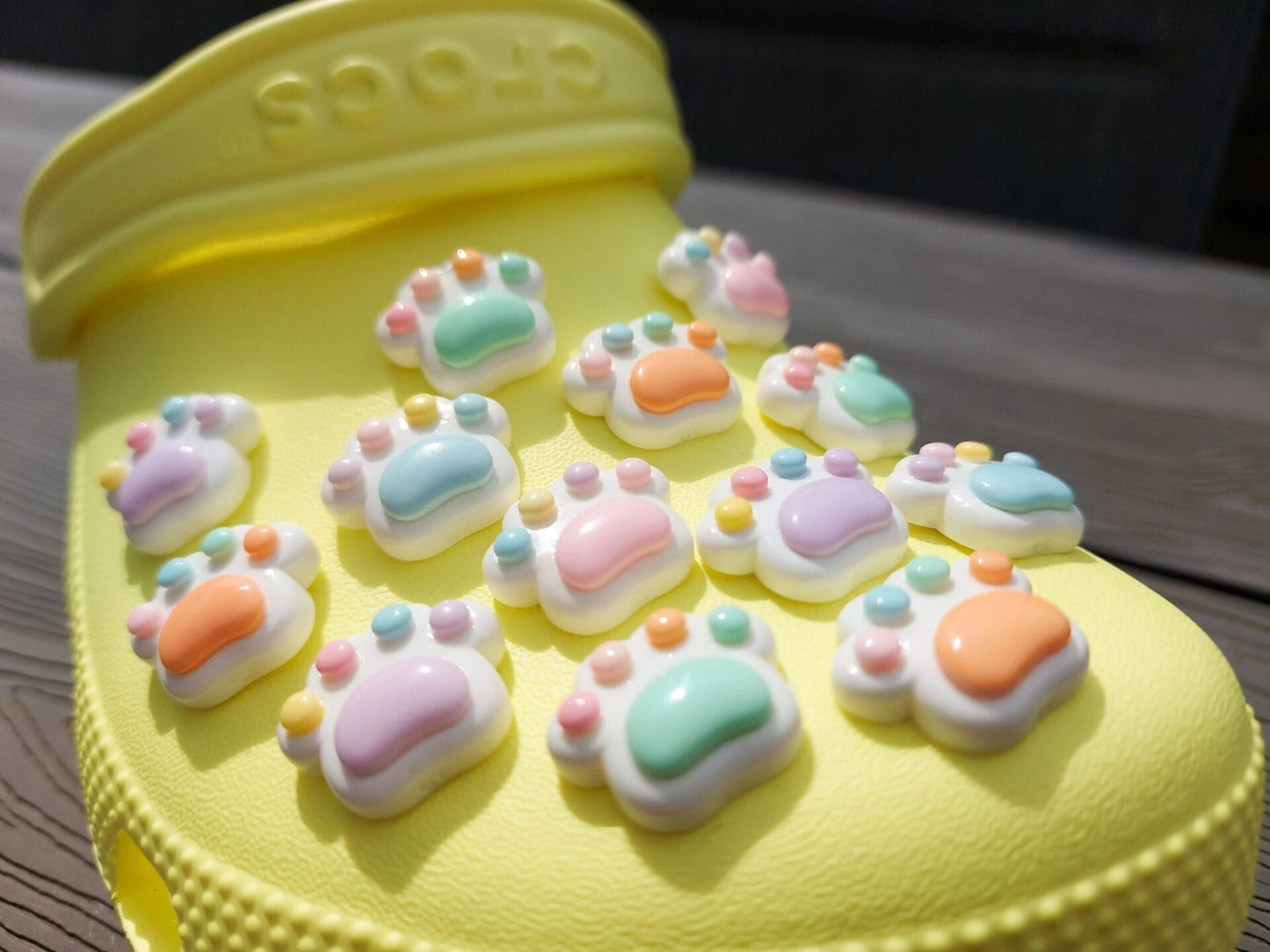 White pawprint charms with pastel-colored footpads on a yellow pair of shoes. These adorable accessories add a cute and playful touch to your footwear, perfect for customizing your shoes with a fun, pet-inspired design.