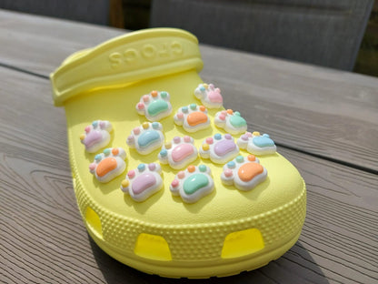 White pawprint charms with pastel-colored footpads on a yellow pair of shoes. These adorable accessories add a cute and playful touch to your footwear, perfect for customizing your shoes with a fun, pet-inspired design.