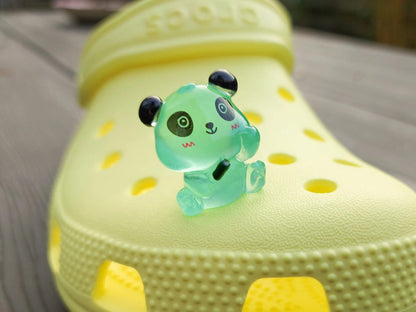 Set of glow in the dark panda shoe charms displayed on a shoe shoe. The charms feature small panda bears in various colors, with a glowing effect. These adorable accessories are designed to light up in the dark.