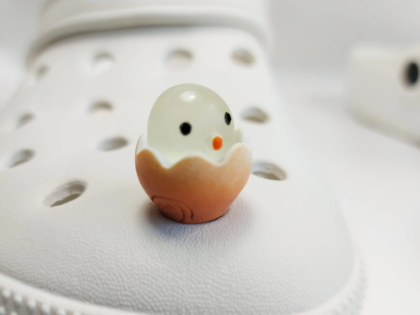 A collection of glow-in-the-dark shoe charms featuring adorable baby chicks nestled in colorful egg shells. Each charm showcases a bright chick in a variety of soft, pastel hues, perfect for adding a fun and playful glow to your shoes at night.