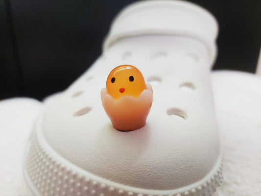 A collection of glow-in-the-dark shoe charms featuring adorable baby chicks nestled in colorful egg shells. Each charm showcases a bright chick in a variety of soft, pastel hues, perfect for adding a fun and playful glow to your shoes at night.