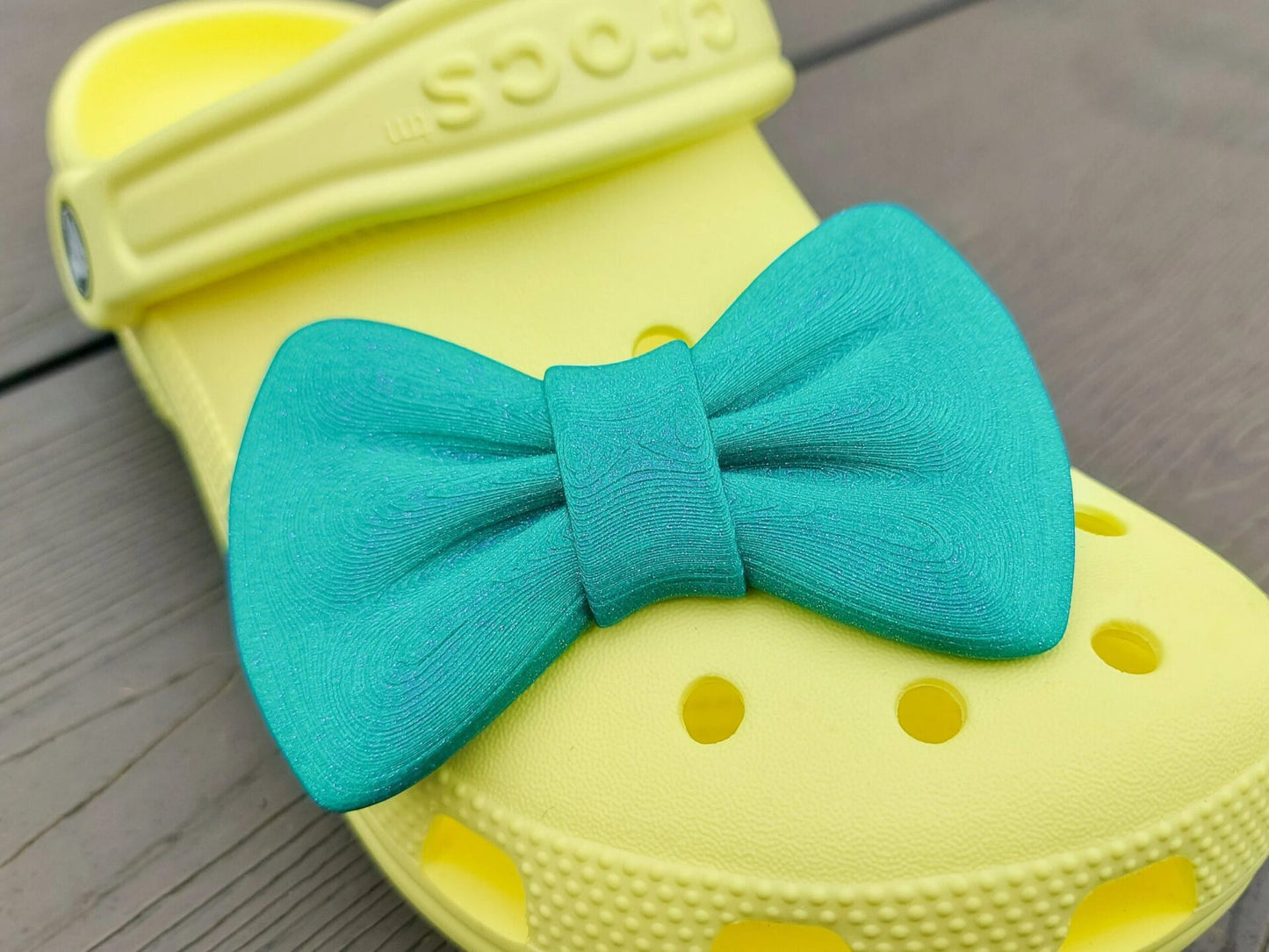 3d-printed bow shoe charms on a pair of shoes shoes. Multiple colors and they have a sparkly glitter.
