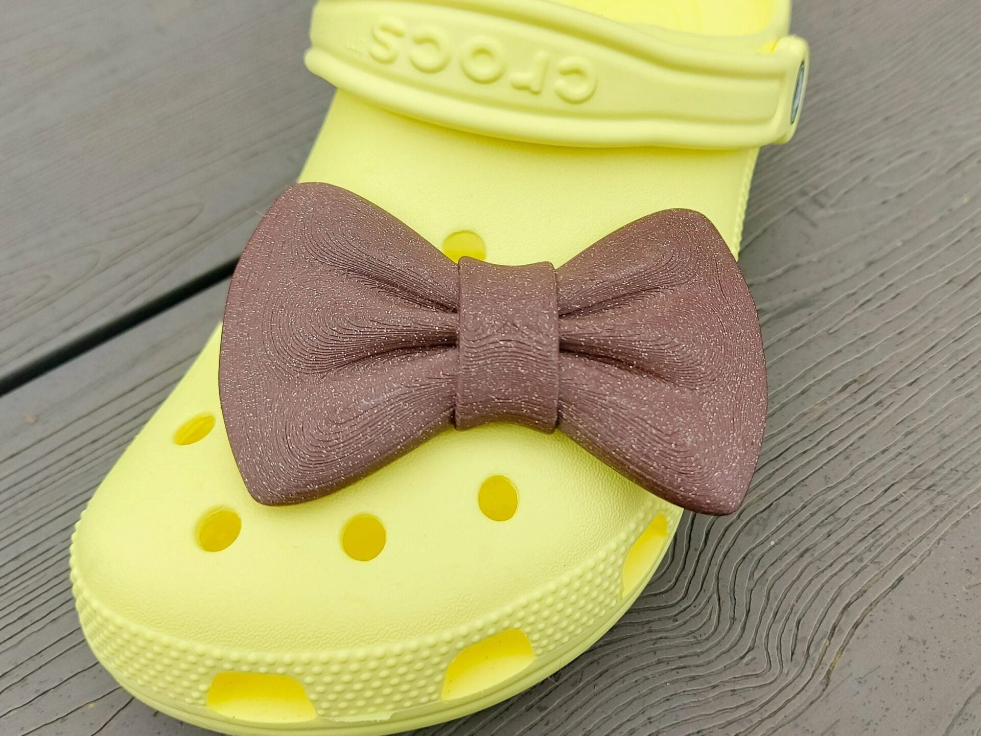 3d-printed bow shoe charms on a pair of shoes shoes. Multiple colors and they have a sparkly glitter.