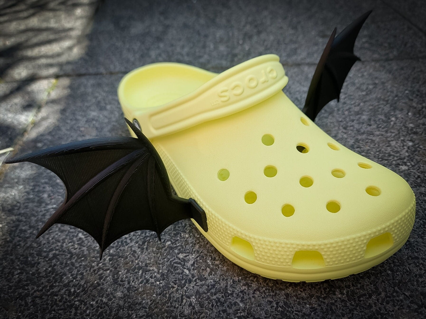 3d-printed bat or dragon wings shoe charms on a pair of shoes shoes. They look halloween themed.