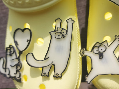Various 3d-printed cartoon cat shoe charms that glow in the dark on a pair of yellow shoes. Each cat has unique features and expressions.