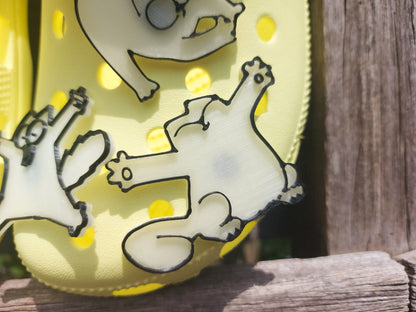 Various 3d-printed cartoon cat shoe charms that glow in the dark on a pair of yellow shoes. Each cat has unique features and expressions.