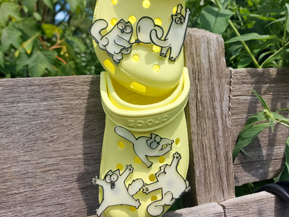 Various 3d-printed cartoon cat shoe charms that glow in the dark on a pair of yellow shoes. Each cat has unique features and expressions.