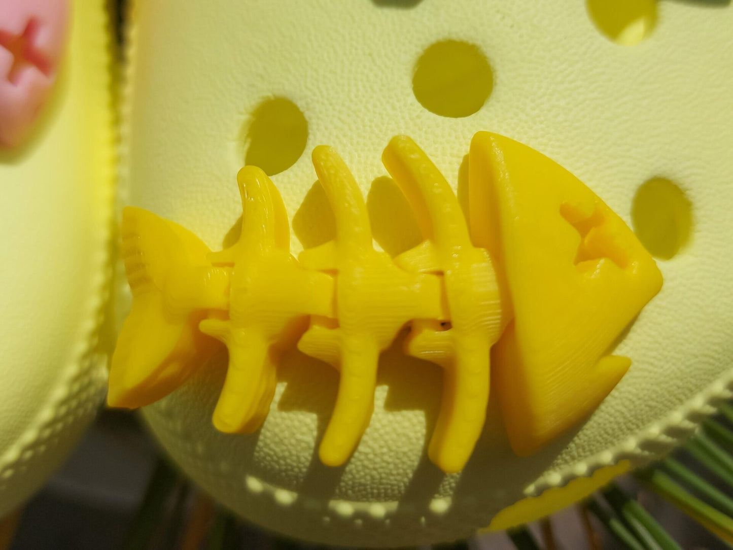 Yellow shoes adorned with colorful 3D-printed articulated fish bone charms in white, pink, black, teal, and yellow, displayed on a grassy background.