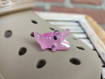 A set of glow-in-the-dark shoeodile charms adorns a shoes shoe. Each charm is shaped like a small, detailed shoeodile, appearing in a range of bright colors that glow vividly in the dark.