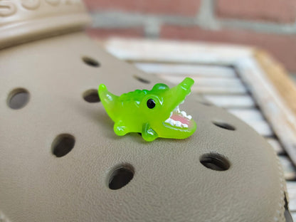 A set of glow-in-the-dark shoeodile charms adorns a shoes shoe. Each charm is shaped like a small, detailed shoeodile, appearing in a range of bright colors that glow vividly in the dark.
