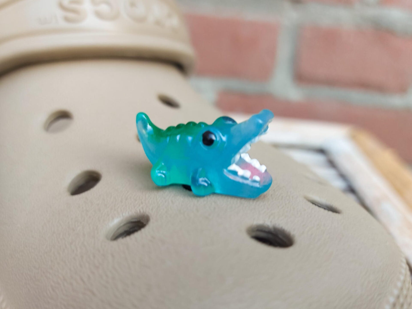 A set of glow-in-the-dark shoeodile charms adorns a shoes shoe. Each charm is shaped like a small, detailed shoeodile, appearing in a range of bright colors that glow vividly in the dark.