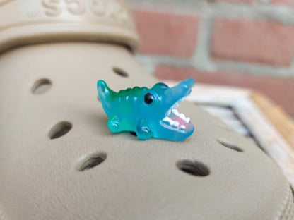 A set of glow-in-the-dark shoeodile charms adorns a shoes shoe. Each charm is shaped like a small, detailed shoeodile, appearing in a range of bright colors that glow vividly in the dark.