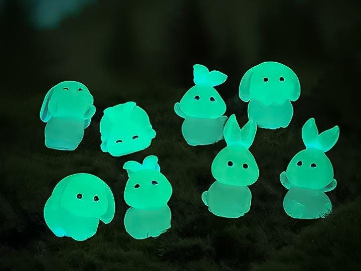 A set of 7 unique glow-in-the-dark bunny charms and 1 carrot charm arranged on a shoe. The bunnies are in various poses, and the carrot sits in the center, all glowing softly in a darkened setting.