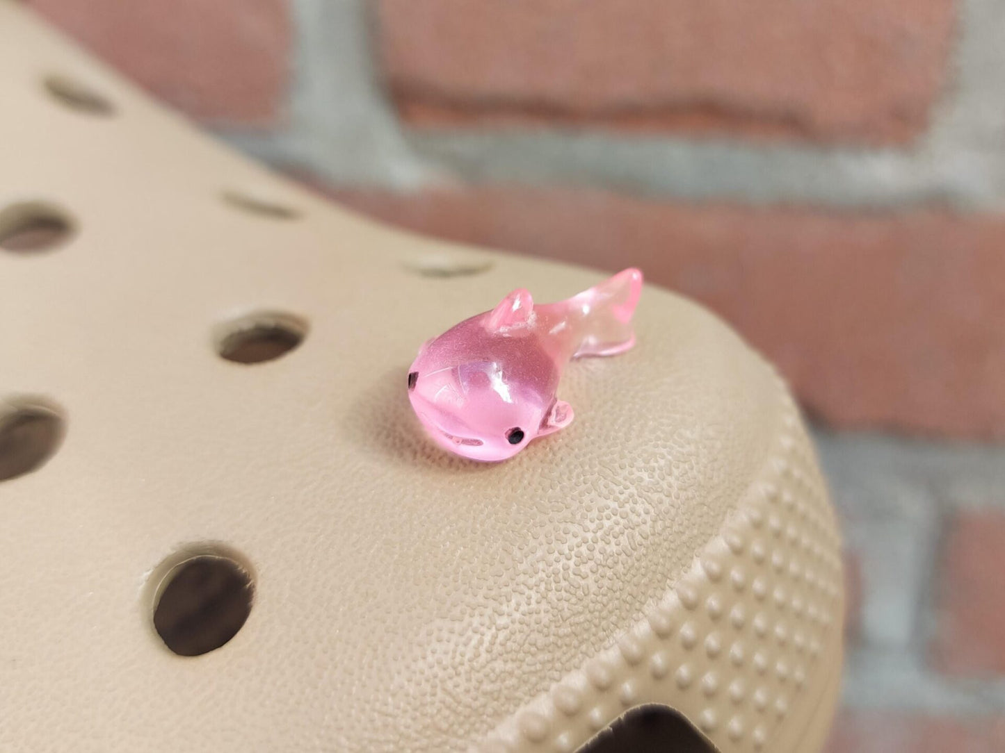 Close-up of glow-in-the-dark shark charms on a shoe shoe, showcasing their detailed design and soft, glowing effect. The sharks are securely attached, and their luminous feature adds a fun, ocean-inspired touch to the shoe in a dark setting.